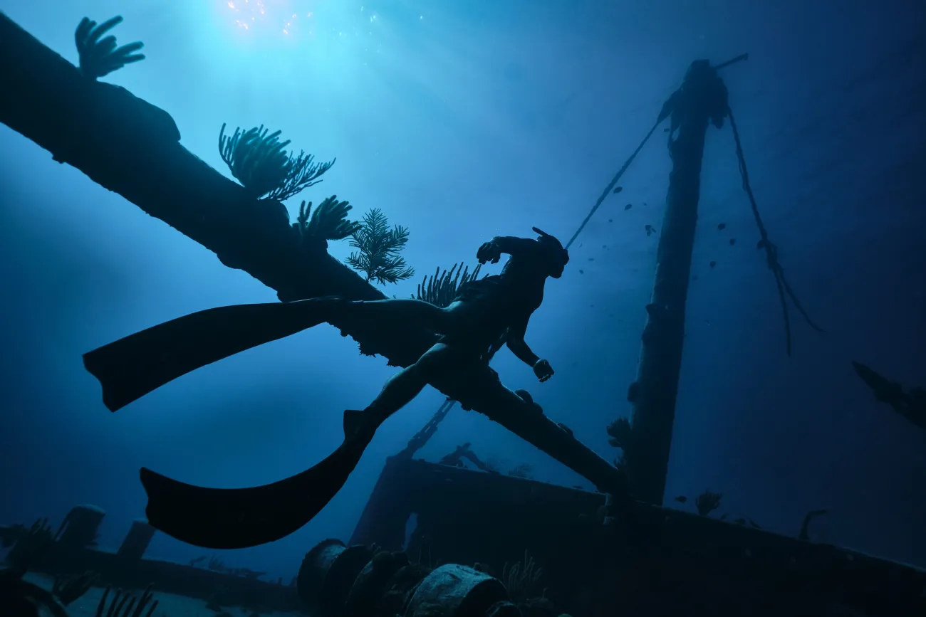 A person is diving underwater swimming next to an old shipwreck.