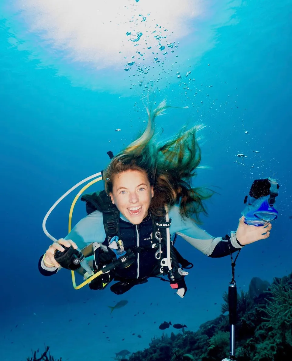 A woman is underwater smiling at the camera.