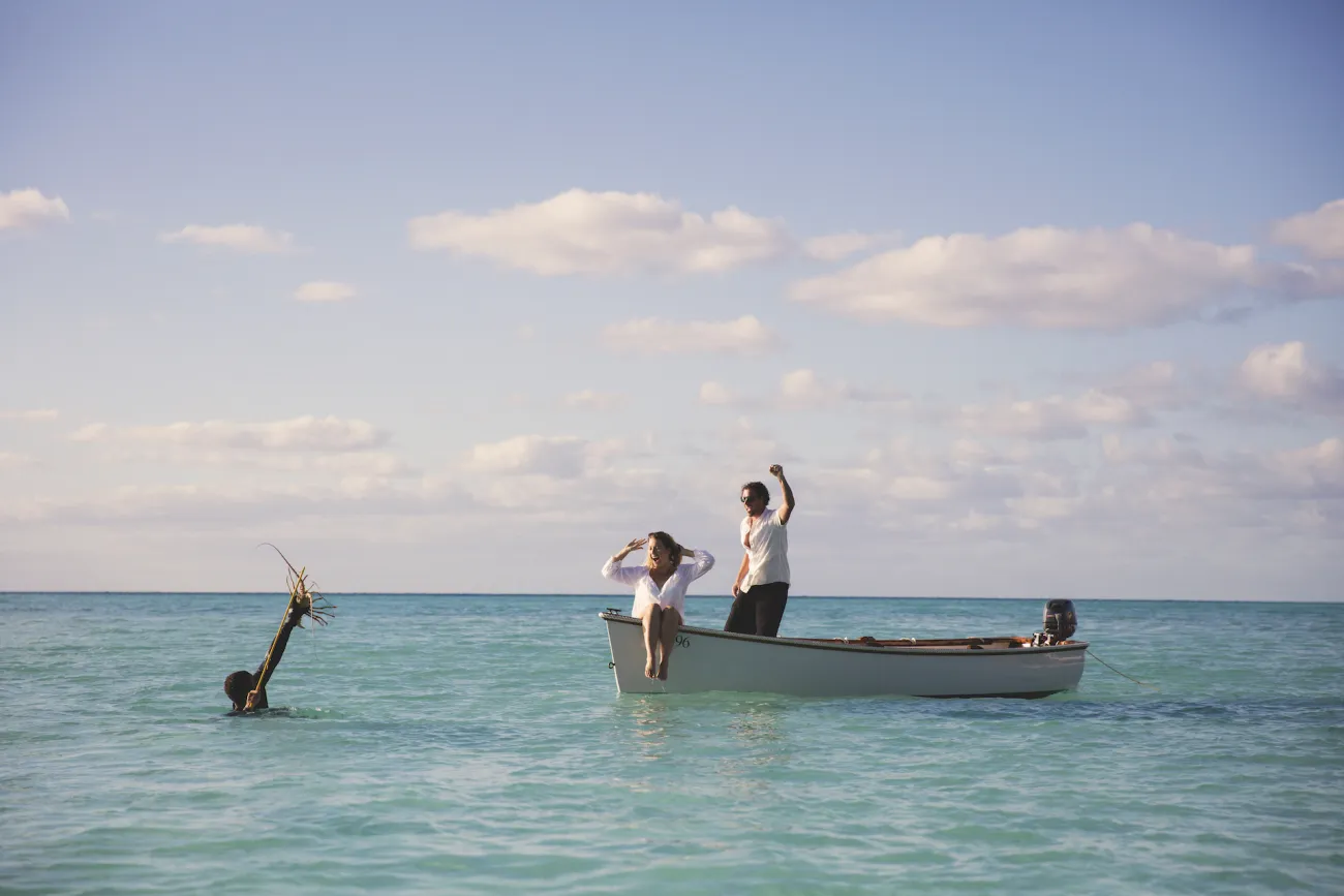 A man fishing for spiny lobster in Bermuda, a couple is cheering from the boat.