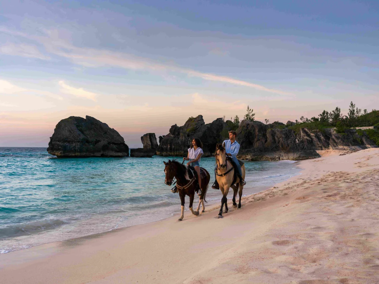Two people are riding horses at sunset on the beach.