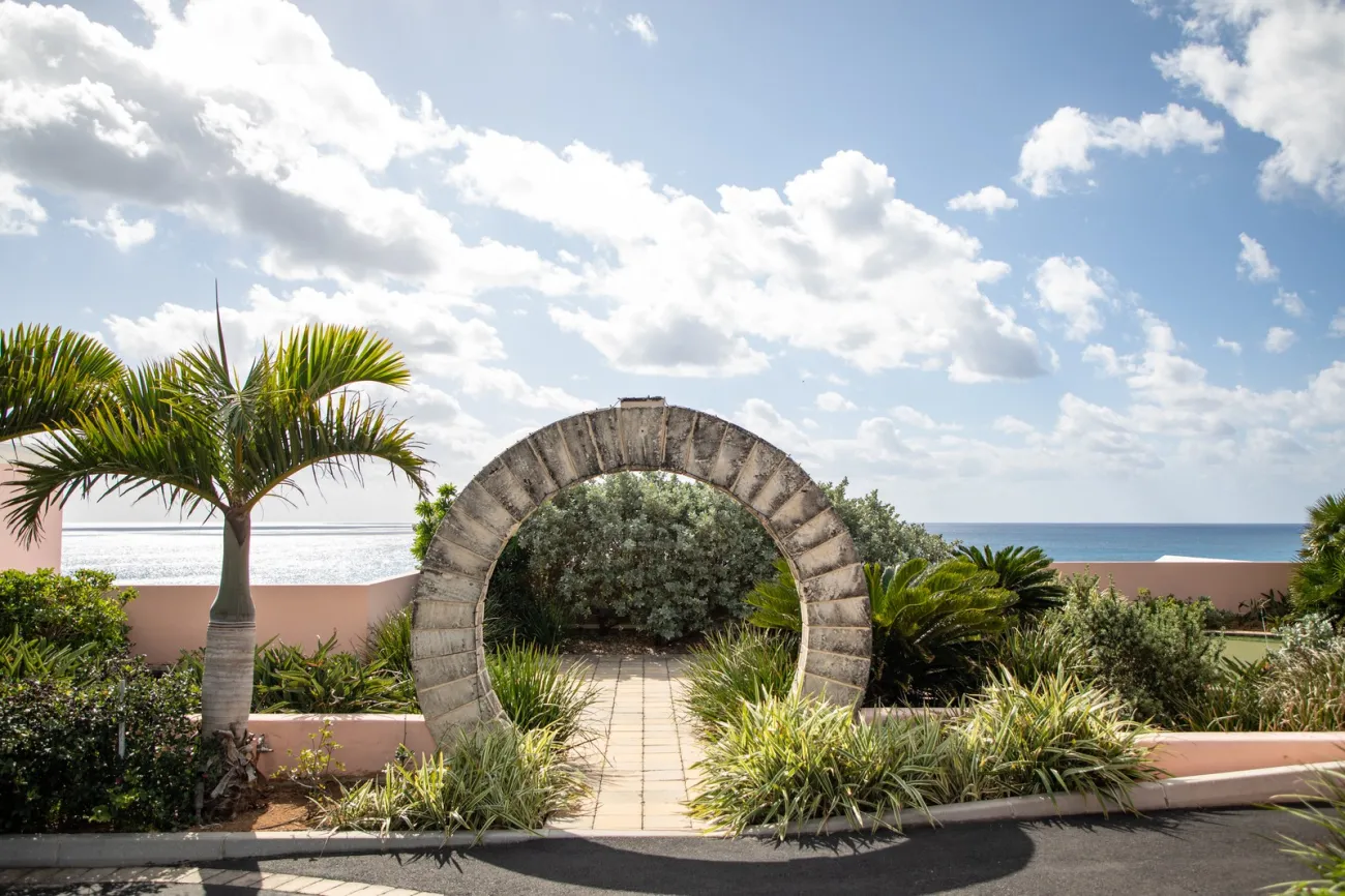 A wide angle of a Bermuda moon gate with calm waters and pink building in the background.