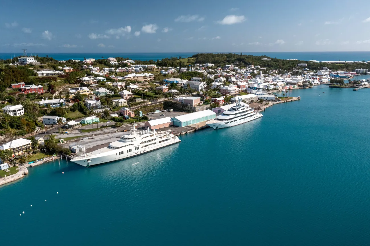 Aerial view of dock with two superyachts and calm blue waters.