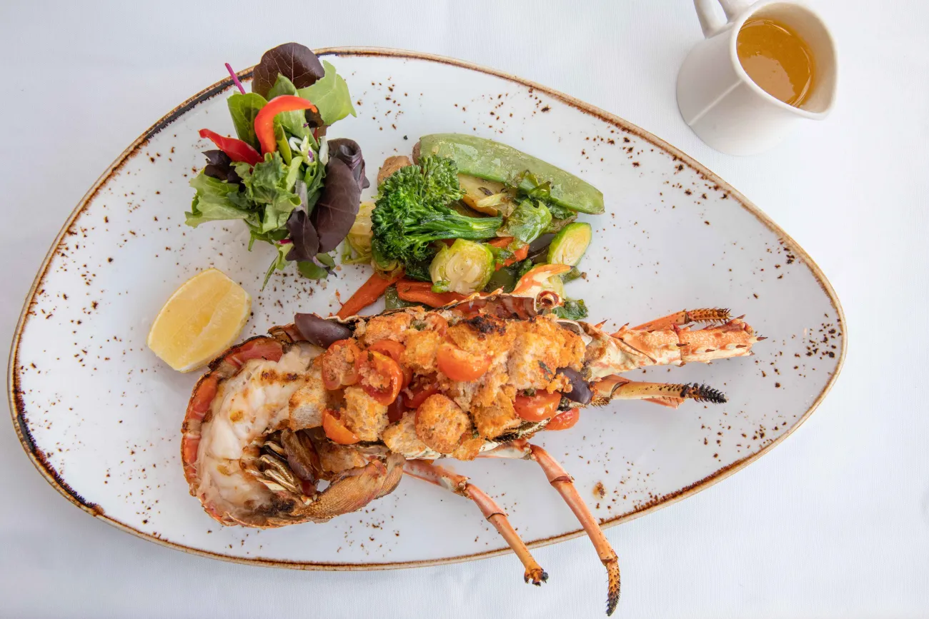 A plate with lobster and vegetables with a butter garlic sauce on the side.