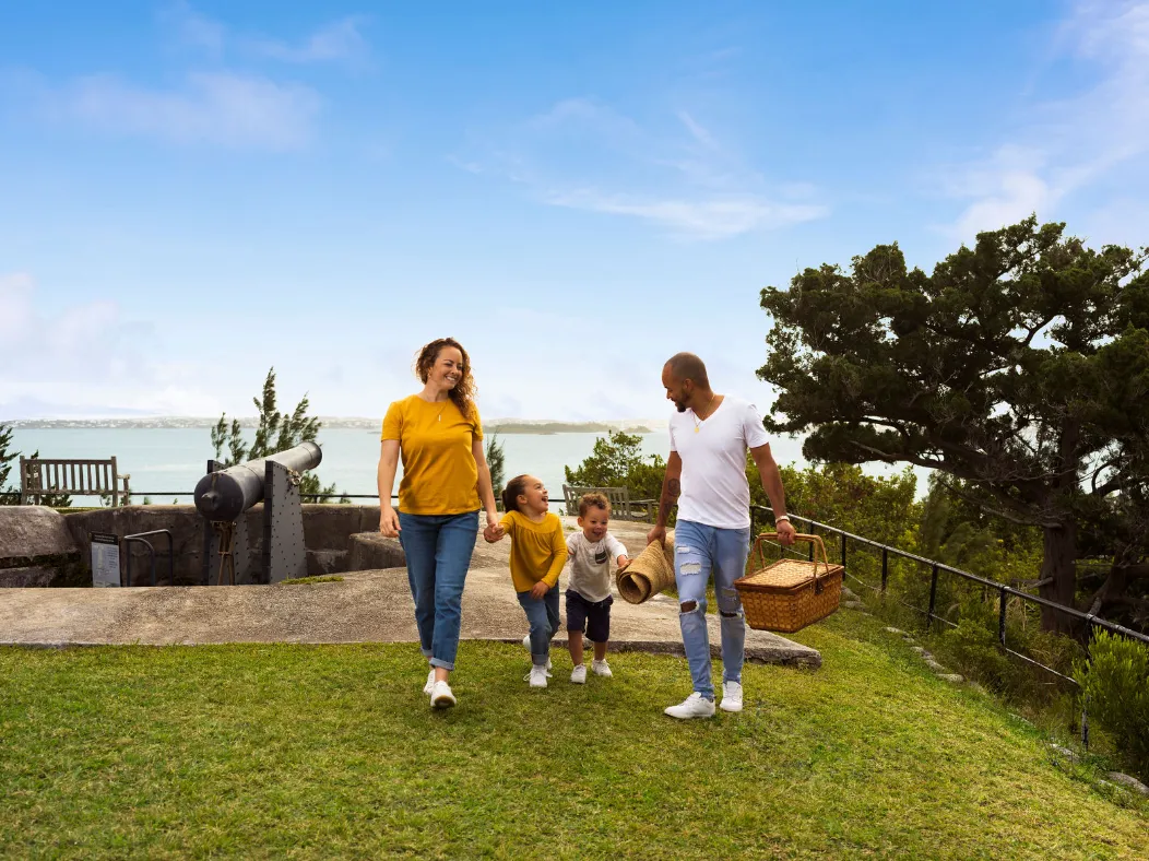 A family is on a hill having a picnic with a scenic ocean view in the background.