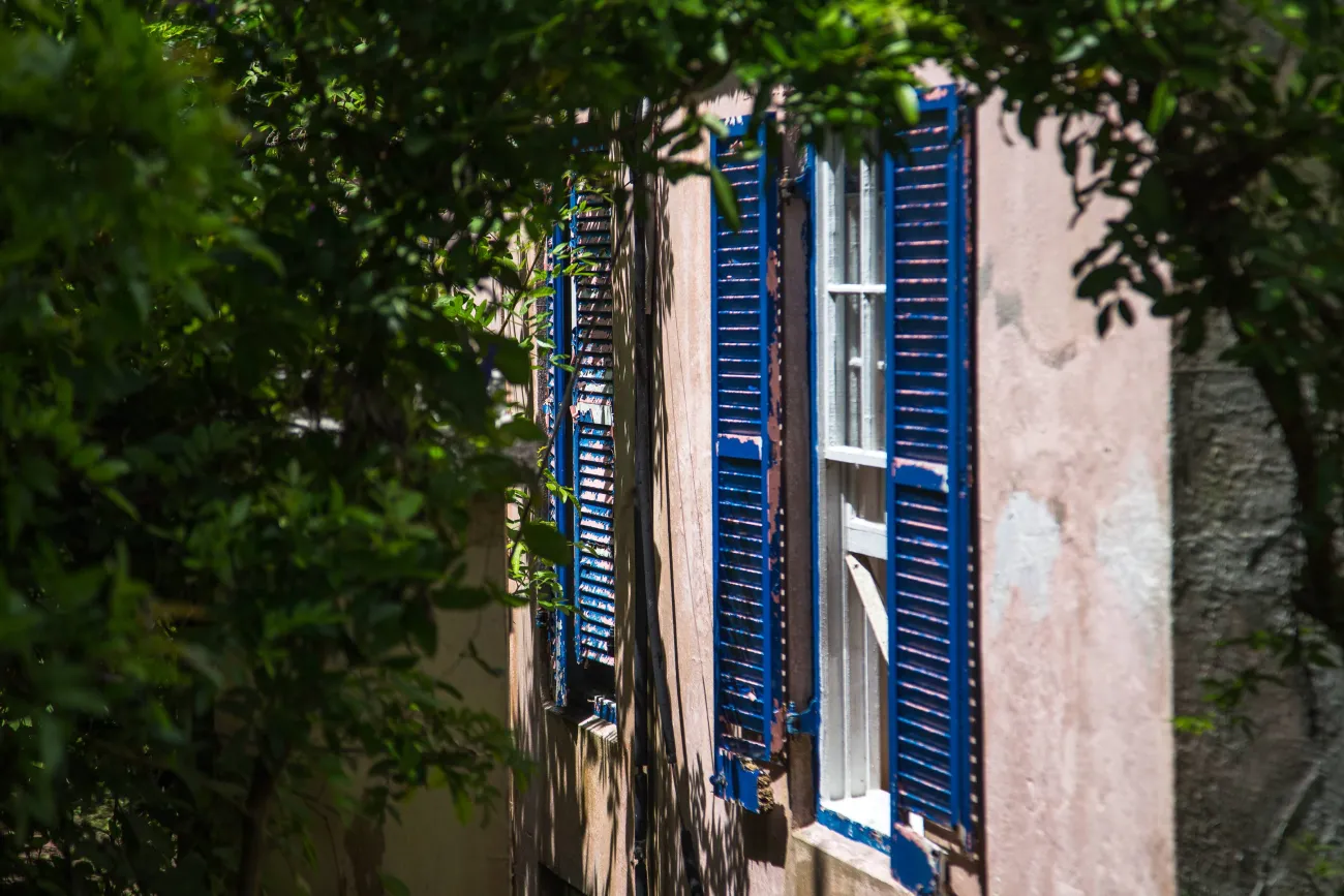 An exterior of an old building with blue shutters and fading pink walls.