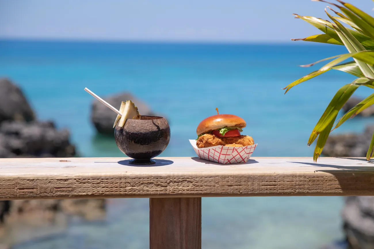 A beach cocktail and a fish sandwich with a waterview in the background