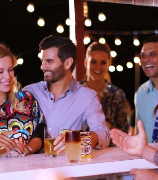 Bar scene with the focus on two girls and one guy laughing with drinks