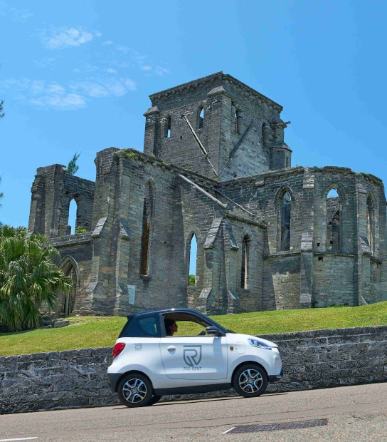 A person is driving an electric microcar by a scenic building.