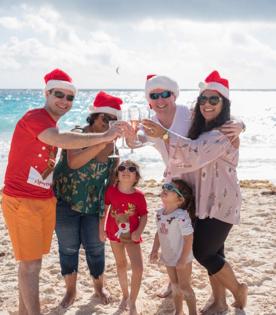 A family is cheering while on the beach in Christmas gear.