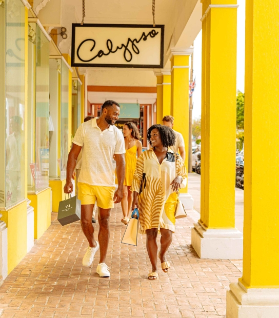 A couple are walking in hamilton by a bright yellow building.