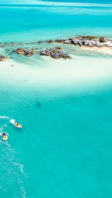 Aerial view of two jet skis riding close to a sandy shore