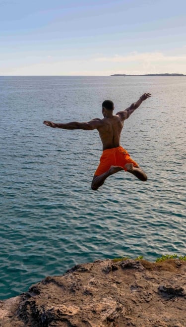 A man is star jumping into the ocean from a cliff.