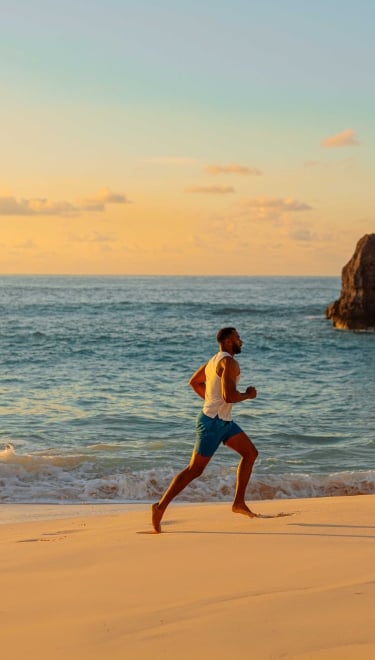 A man is running at sunrise on a empty beach with calm ocean waters in the background.