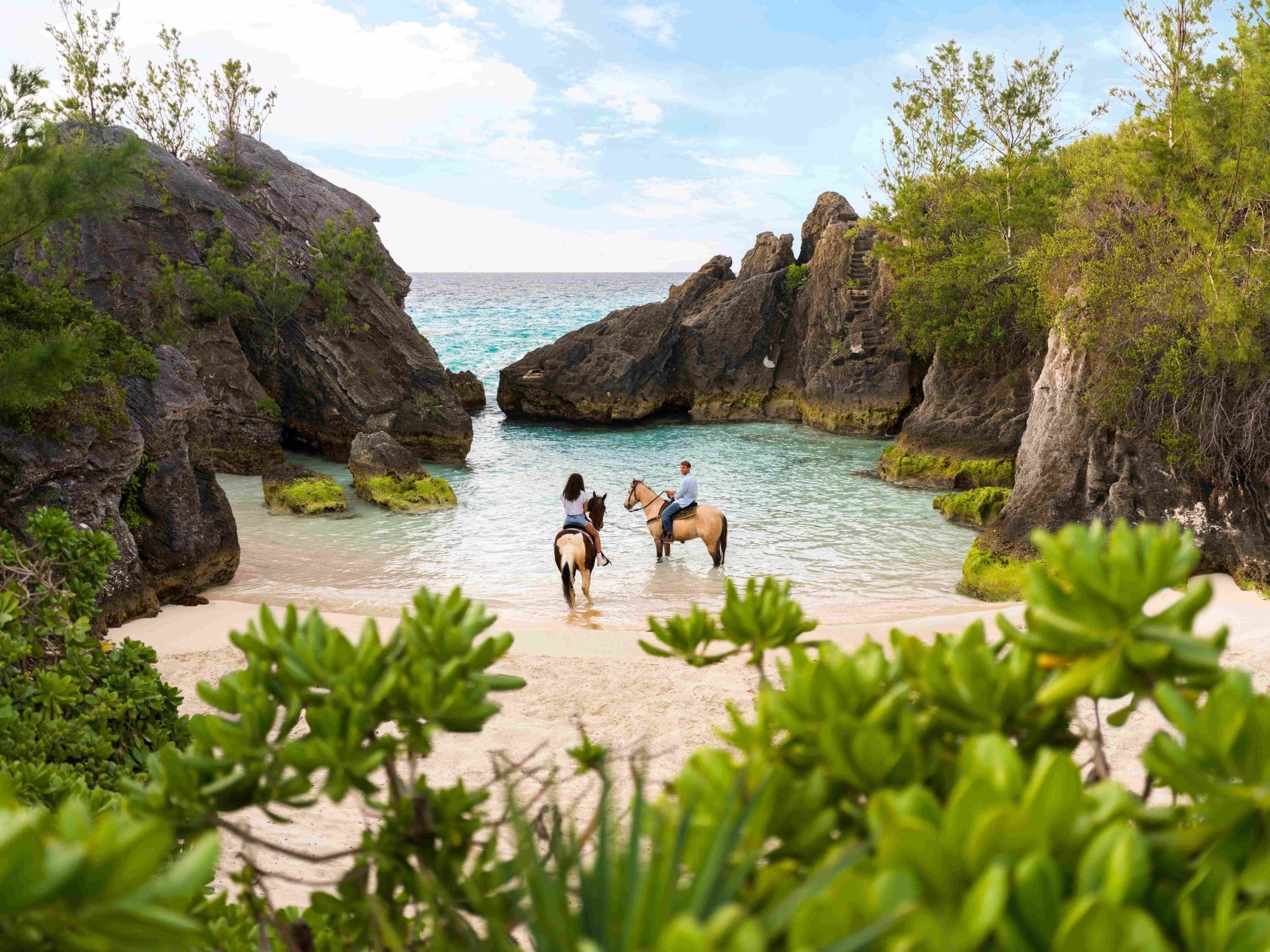 A couple are on horses in a secluded beach.