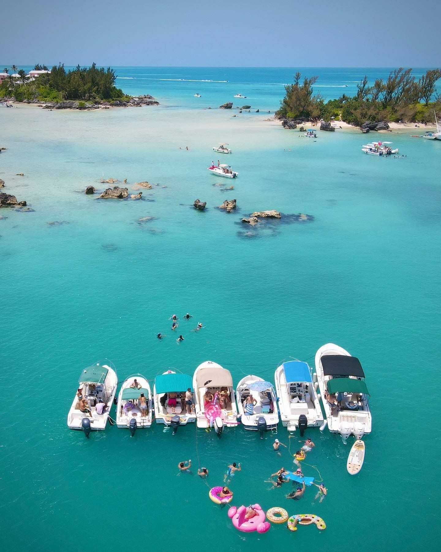 A line of boats in blue water with people swimming around them