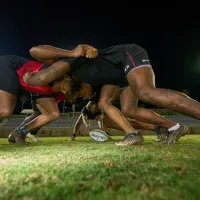 A rugby team practices a scrum under the lights at night at the Bermuda National Sports Centre
